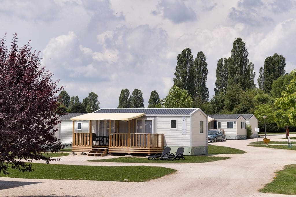 Des emplacements grand confort en pleine nature
Pour les amoureux du camping traditionnel, le domaine propose 261 emplacements spacieux (110 m² en moyenne), ensoleillés ou ombragés selon vos préférences. Tous les emplacements grand confort sont équipés de l'électricité 10A, d'un accès à l'eau et de l'évacuation des eaux usées.
Des locations de mobil-homes, chalets et roulottes
Côté locatif, le camping met à disposition 47 hébergements aux gammes variées, pour 4 à 6 personnes :
Les Roulottes : un hébergement insolite pour 4 personnes, avec chambre, salle d'eau, coin kitchenette et terrasse extérieure. L'originalité du séjour bohème, avec le confort en plus.
Les mobil-homes : pour les familles en quête de confort et d'un bon rapport qualité-prix. Cuisine équipée, TV, salle de bain, WC séparés et terrasse couverte. Choisissez un modèle 2 ou 3 chambres pour 4 à 6 personnes. Le mobil-home Premium dispose de la climatisation et d'un jacuzzi privatif.
Camping du Lac d'Orient avec mobil-homes alignés sous les arbres, ambiance nature et calme